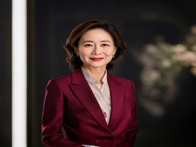 美熟母创始人陈雅琳女士，身着酒红色职业装，面带自信微笑，站在品牌展示墙前，气质成熟优雅，彰显专业品牌领导力